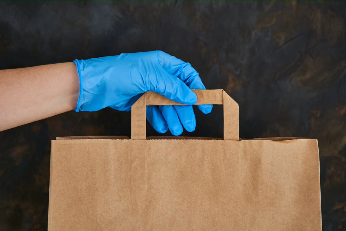 Courier in gloves delivering a paper bag of supplies to a recipient